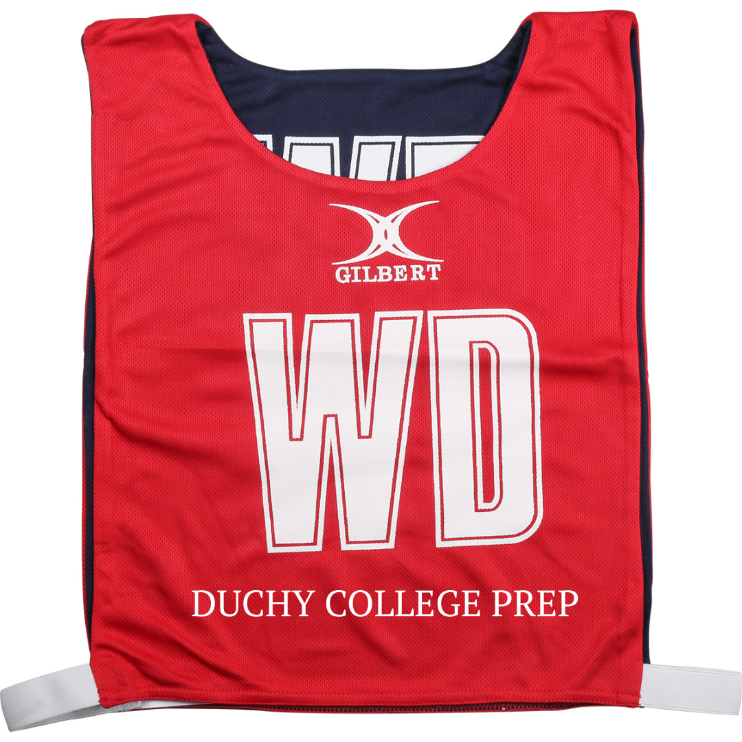 Introducing the Personalised Gilbert Netball Bibs (Reversible) by Gilbert—a red sports bib featuring the iconic GILBERT logo, bold white WD letters, and “DUCHY COLLEGE PREP” printed along the bottom. Designed with black sides and adjustable white straps for a comfortable fit, this reversible bib is an excellent choice for school netball teams looking for top-quality netball gear.