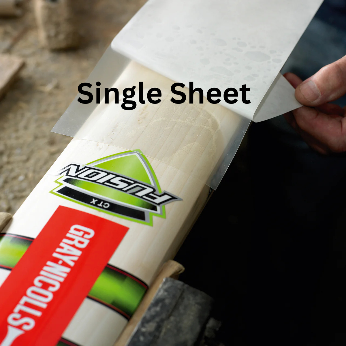 A person applies a Gray-Nicolls Extratec self-adhesive facing to a Gray Nicolls Fusion GT-X cricket bat on a workbench for added protection.