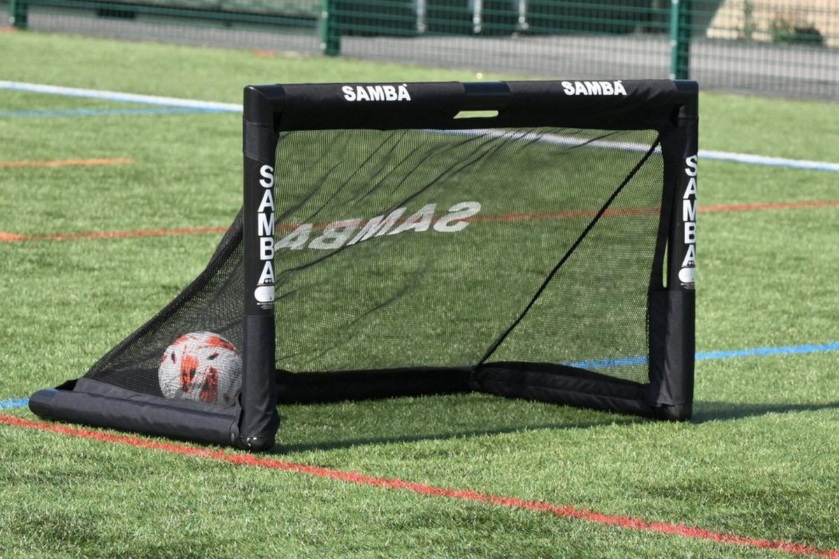 A Samba Sports 4ft x 2.5ft Folding 3v3 Goal with a black frame is set on artificial turf. A soccer ball sits inside the net, while blue and red field lines mark the pitch—perfect for quick 3v3 games or training sessions.