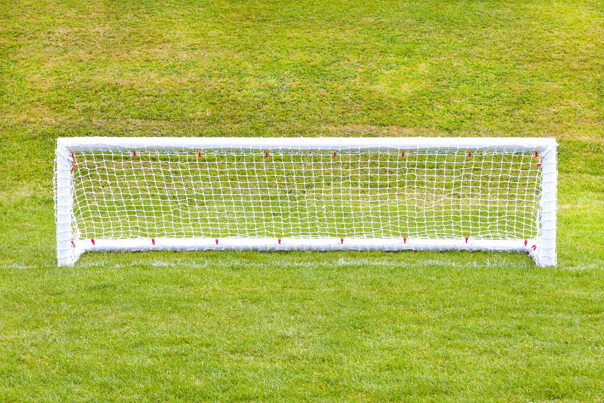 A pair of 8ft x 2ft Mini Hockey Goals by Samba Sports, complete with nets, stands on a green grassy field. The well-maintained turf behind the goals is slightly elevated.