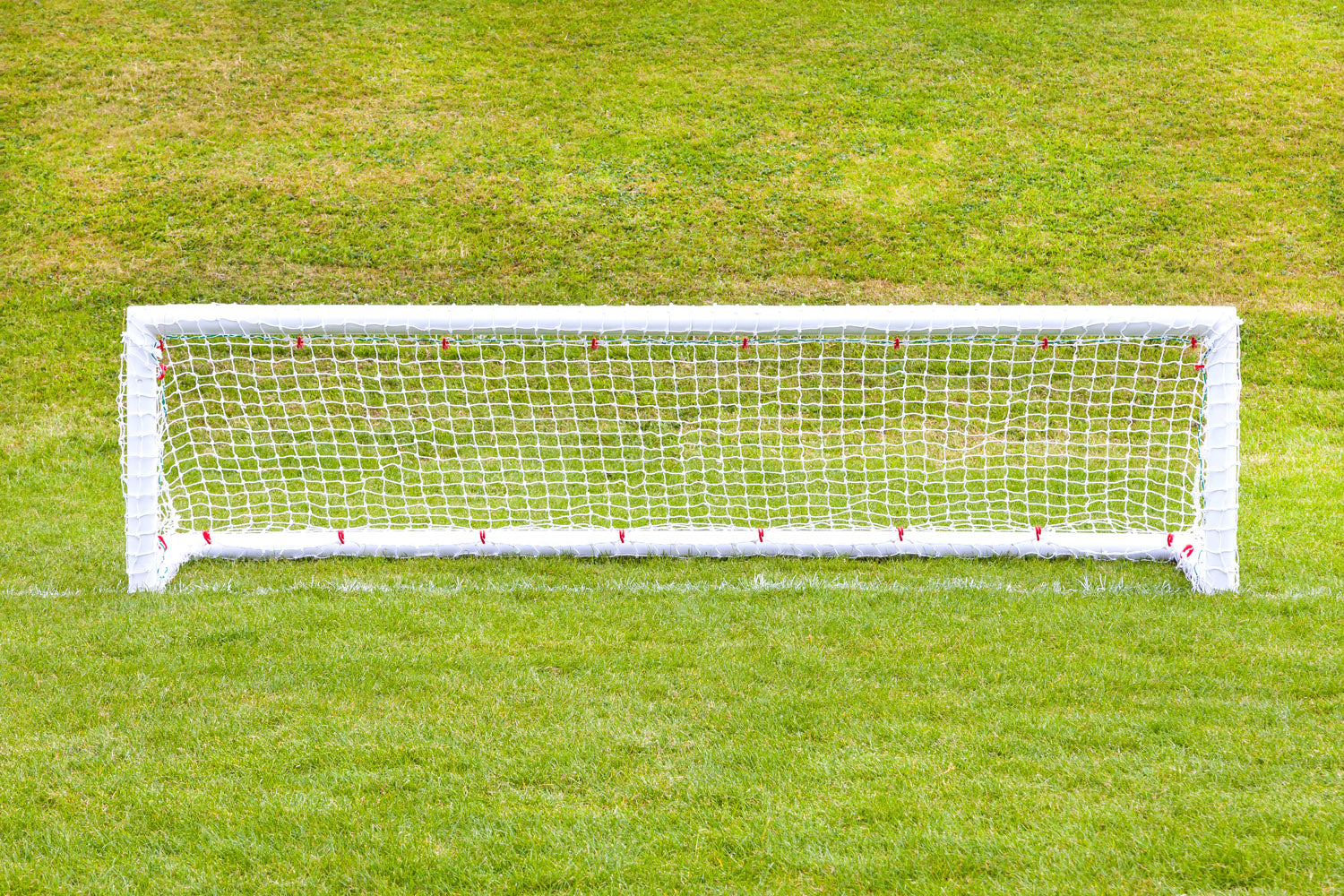 A pair of 8ft x 2ft Mini Hockey Goals by Samba Sports, complete with nets, stands on a green grassy field. The well-maintained turf behind the goals is slightly elevated.