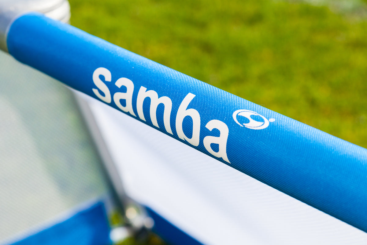 Close-up of a blue Samba Sports Aluminium Folding Football Goal (3v3, 4ft x 2.5ft) with white "samba" text and logo, shown with grass and net blurred in the background.