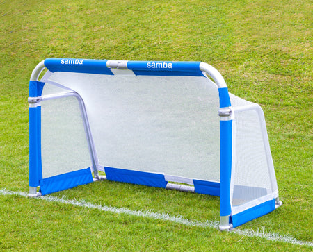 A Samba Sports 3v3 4ft x 2.5ft Aluminium Folding Football Goal with blue and white frame and net is placed on green grass near a white line, featuring the word "samba" on its aluminium top frame.