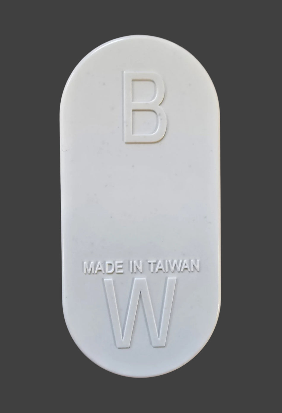 A white, oval tablet resembling a Gray Nicolls Umpires Counter, showing "B" at the top, "MADE IN TAIWAN" in the center, and "W" at the bottom, is displayed against a dark gray background. Brand: Gray Nicolls.