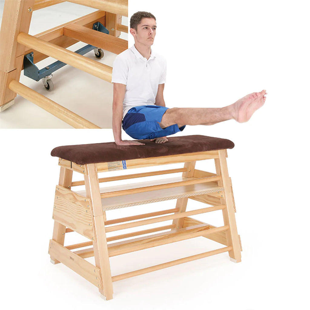 A man in a white shirt and blue shorts balances with straight legs elevated on a Niels Larsen Vaulting Bar Box - Hide Top by Niels Larsen, which features side rungs and a padded natural hide top.