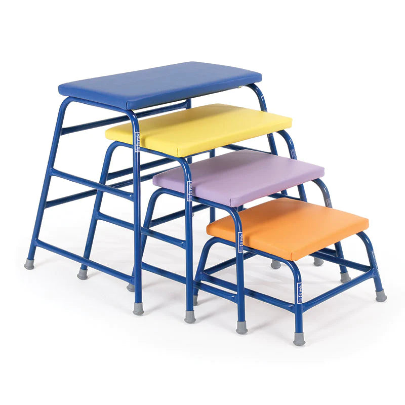 The Niels Larsen Agility Table set by Niels Larsen includes four platforms with powder-coated steel frames and colorful tops—blue, yellow, purple, and orange—each with a foam padded surface, arranged from shortest to tallest.