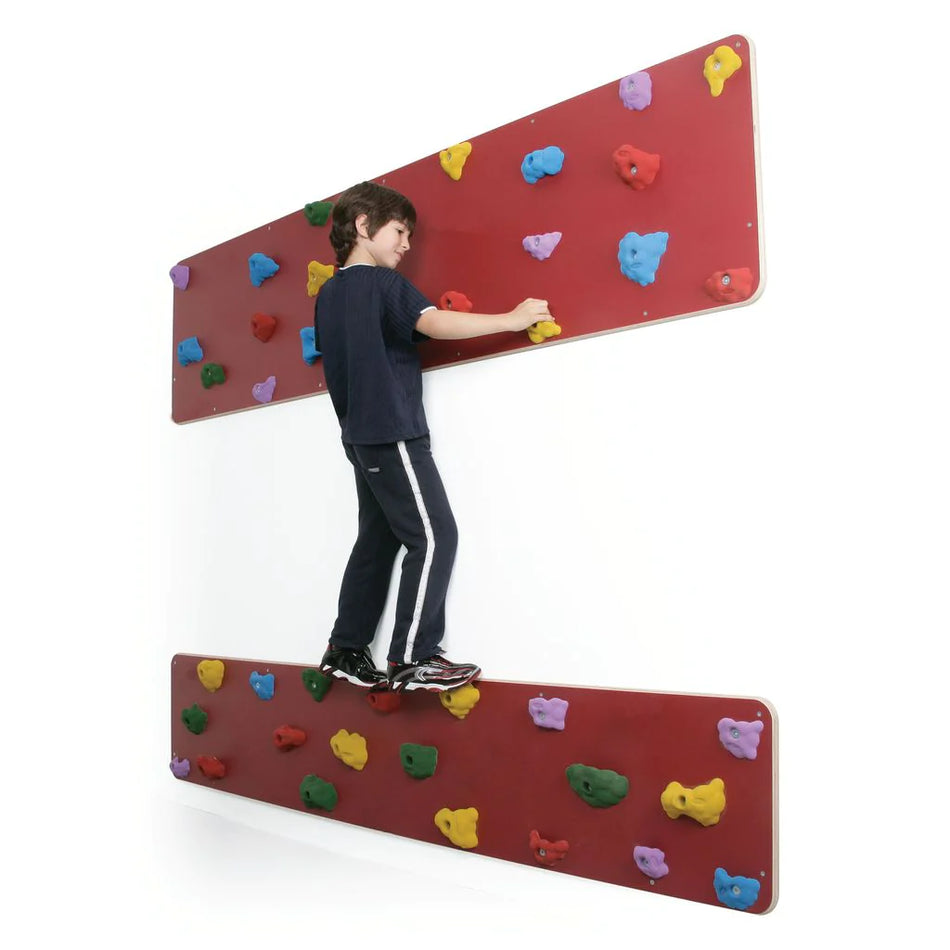 A young boy climbs sideways on Niels Larsen 2Traverse Panels by Niels Larsen, featuring red, UV-resistant climbing panels with colorful hand and footholds, mounted on a white wall.