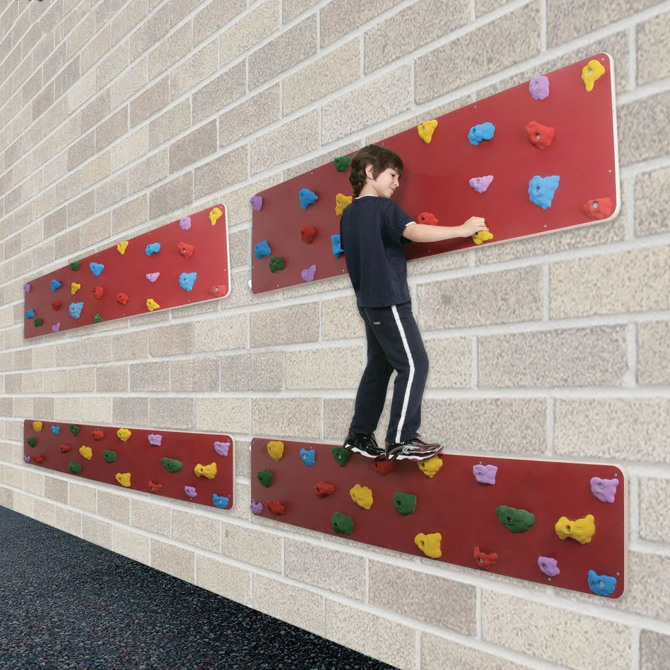 A child climbs sideways on a Niels Larsen 2Traverse Panel, a UV resistant, colorful indoor climbing wall from Niels Larsen, attached to a brick wall.