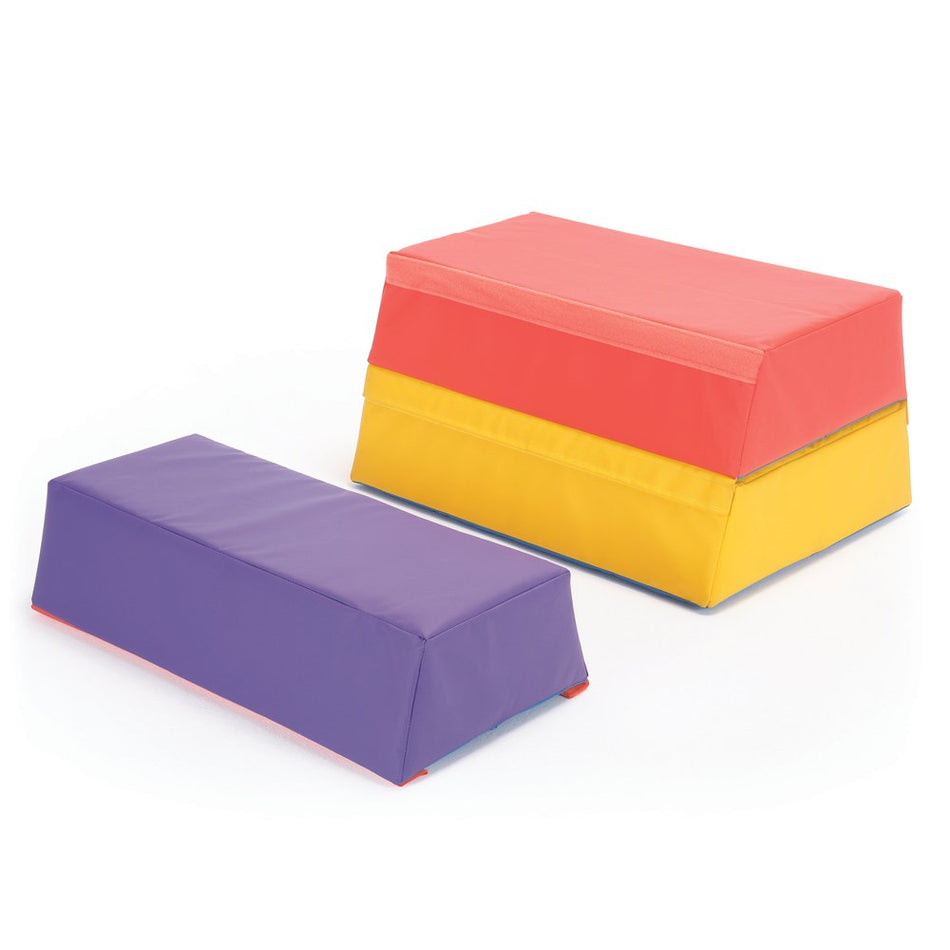 Two padded foam gym blocks from Niels Larsen: a purple Activsoft 3 Section Vault Box and a stacked block in yellow, orange, and red. Both have smooth, wipeable surfaces and are shown on a white background.