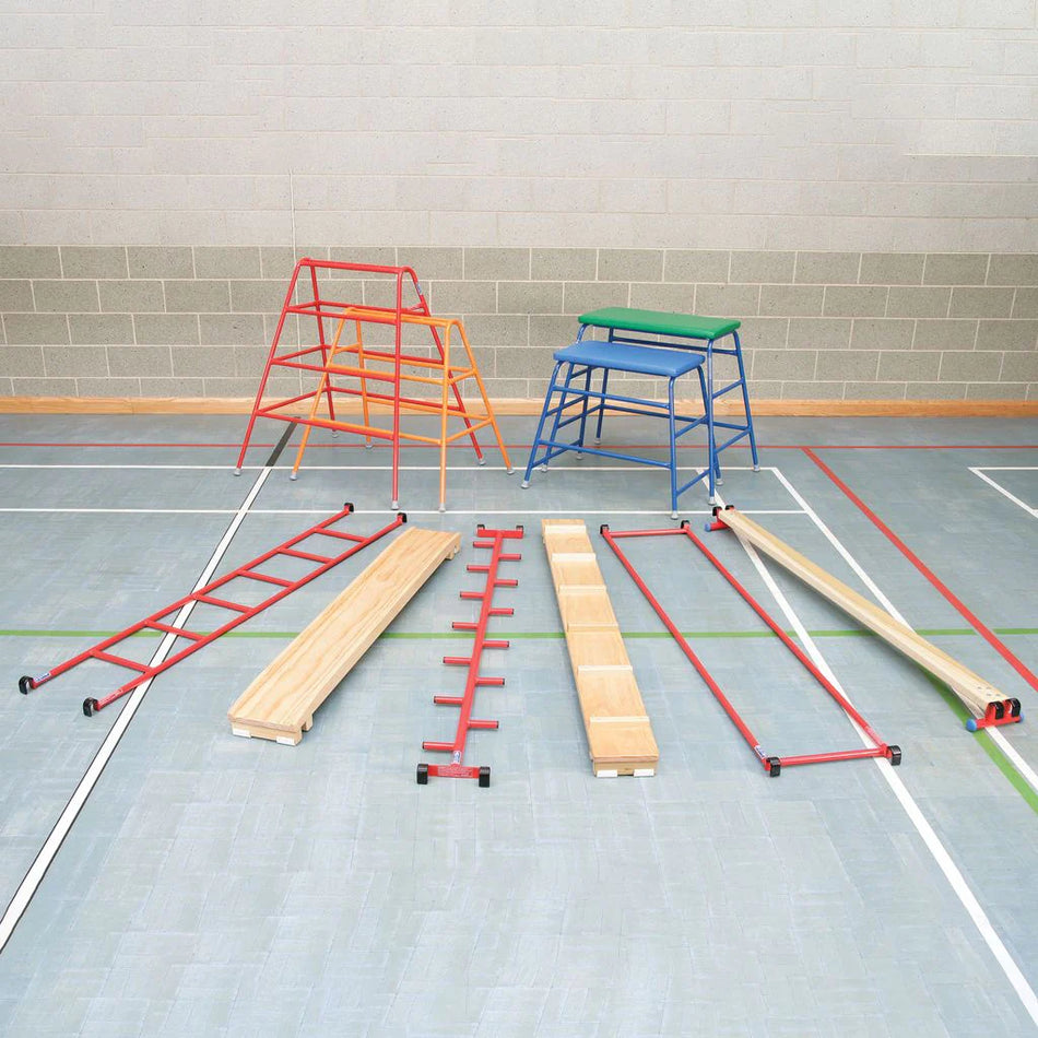 A school gym featuring Niels Larsen Agility Set equipment, including timber balance beams, red and blue metal frames, and red ladders, all arranged on a light blue floor marked with white and red court lines.