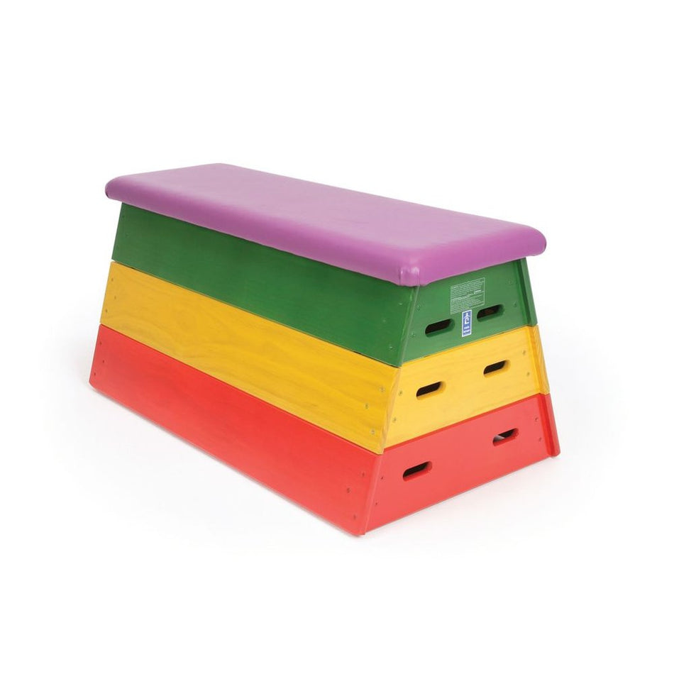 The Niels Larsen Activvault by Niels Larsen is a rectangular vault box with stacked red, yellow, and green sections and a purple padded vinyl top. Each section features side handles for easy transport, making it ideal for gymnastics training.
