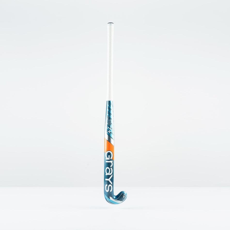 The Grays JB 7+ Junior Hockey Stick 2026, in blue and orange with Graphene technology for drag-flicking control, stands upright against a plain white background with the Grays logo visible.