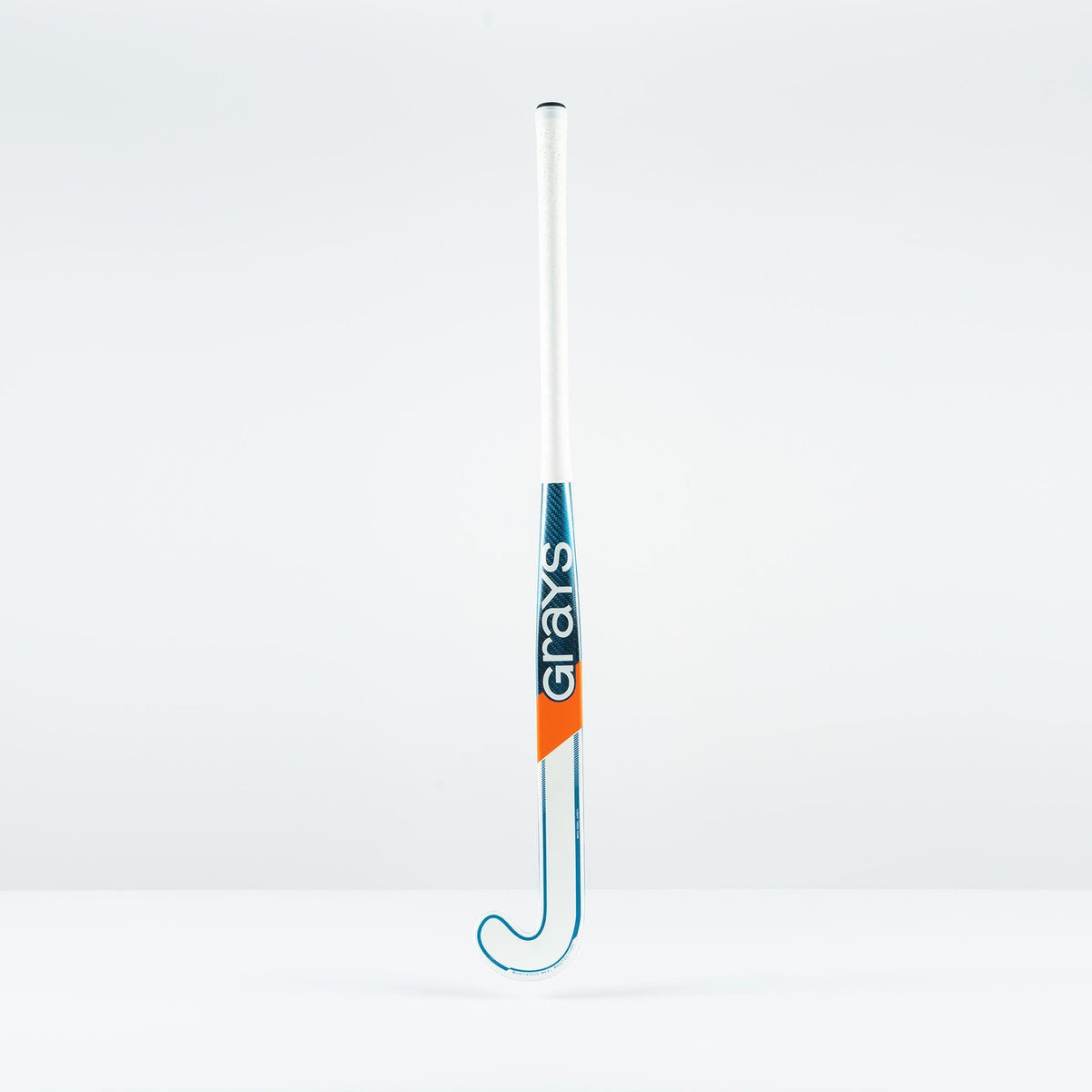 The Grays JB 7+ Junior Hockey Stick 2026 has a white handle, blue and orange accents, the Grays logo printed vertically, and uses Graphene technology for intermediate power and better drag-flicking control against a plain background.