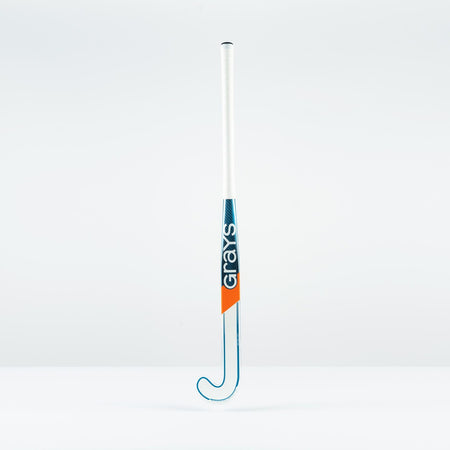 The Grays JB 7+ Junior Hockey Stick 2026 has a white handle, blue and orange accents, the Grays logo printed vertically, and uses Graphene technology for intermediate power and better drag-flicking control against a plain background.