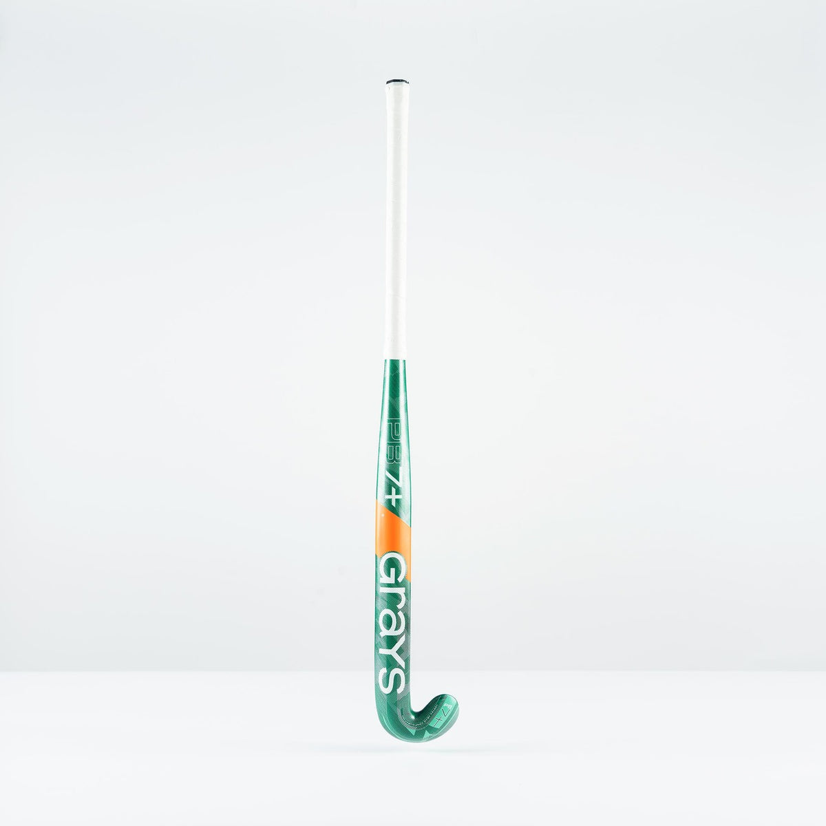 A green and white Grays PB 7+ Junior Hockey Stick 2026 with orange accents stands upright against a plain white background, displaying the brand name and offering intermediate power plus supreme control.