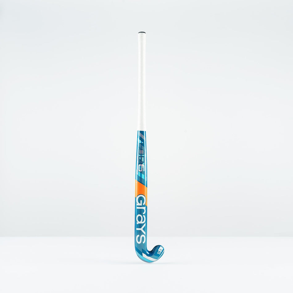 The Grays JB 6 Junior Hockey Stick 2026, in blue, white, and orange, designed for drag-flicking, stands upright against a plain white background.