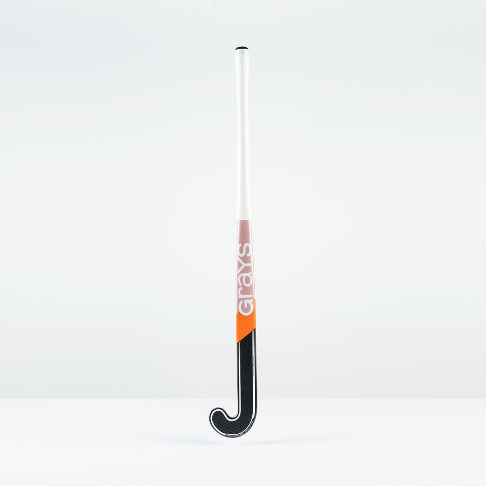 The Grays JB 4 Junior Hockey Stick 2026, featuring a white handle, orange and pink Grays branding, and a black curved end for drag-flicking, stands upright against a plain white background.