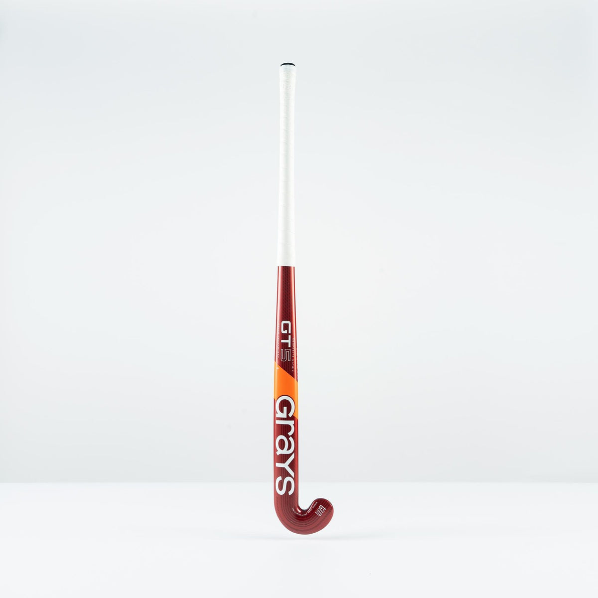 The Grays GT 5 Junior Hockey Stick 2026, featuring a red and white design with a high bow apex and bold Grays branding, stands upright against a plain white background.