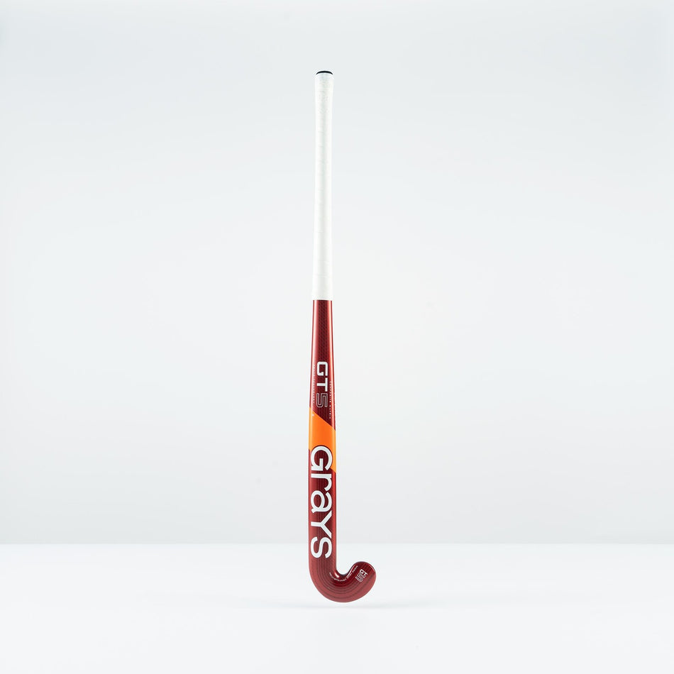 The Grays GT 5 Junior Hockey Stick 2026, featuring a red and white design with a high bow apex and bold Grays branding, stands upright against a plain white background.