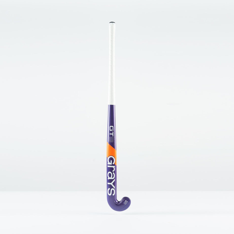The Grays GT 3 Junior Hockey Stick 2026, in purple with a white grip and orange accents, displays the Grays brand on the shaft. Designed for balanced power and control, it stands upright against a plain white background.