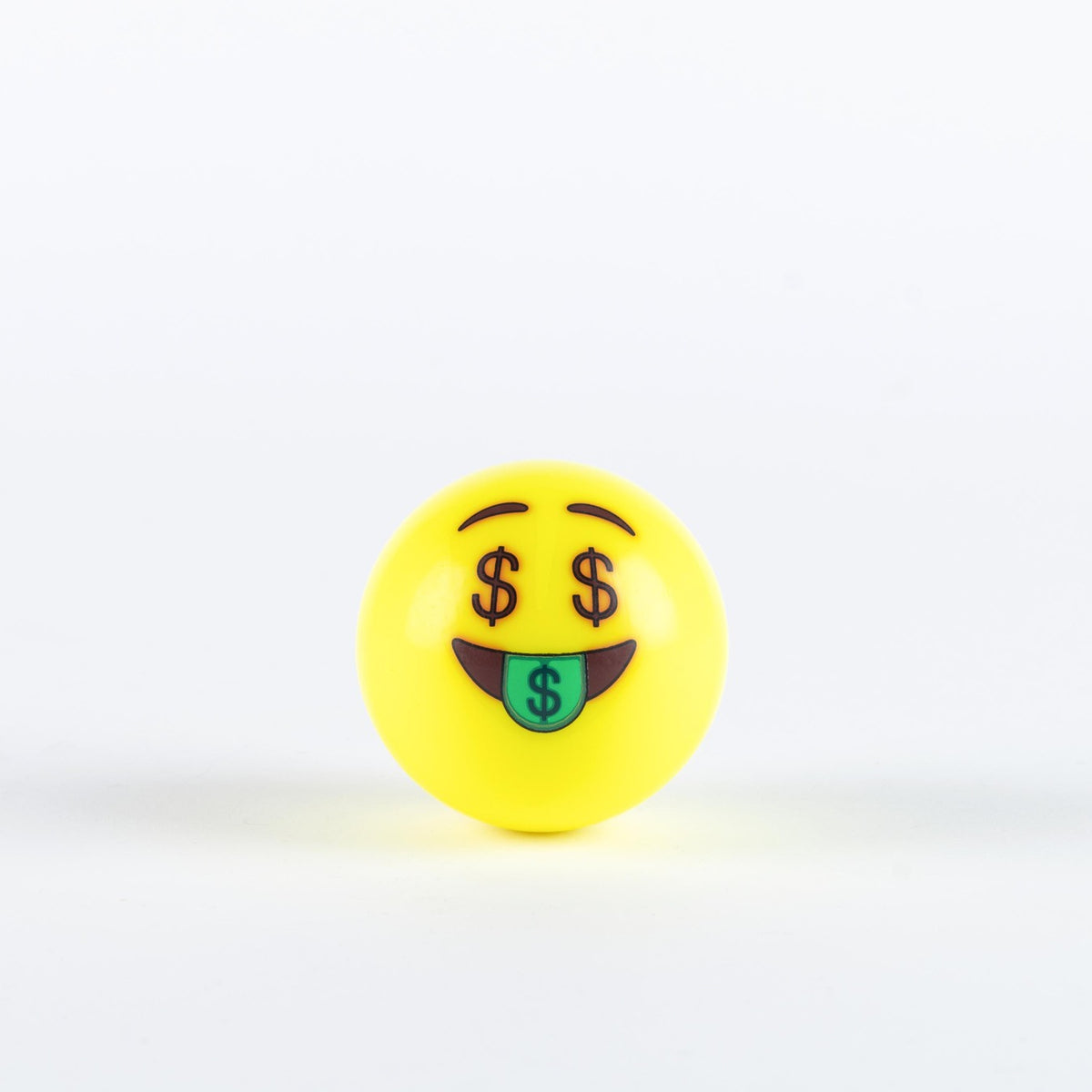 The Grays Emoji Hockey Ball by Grays features a yellow ball with an emoji face showing dollar sign eyes and a green tongue with a dollar symbol—ideal as a 2025 hockey player gift.