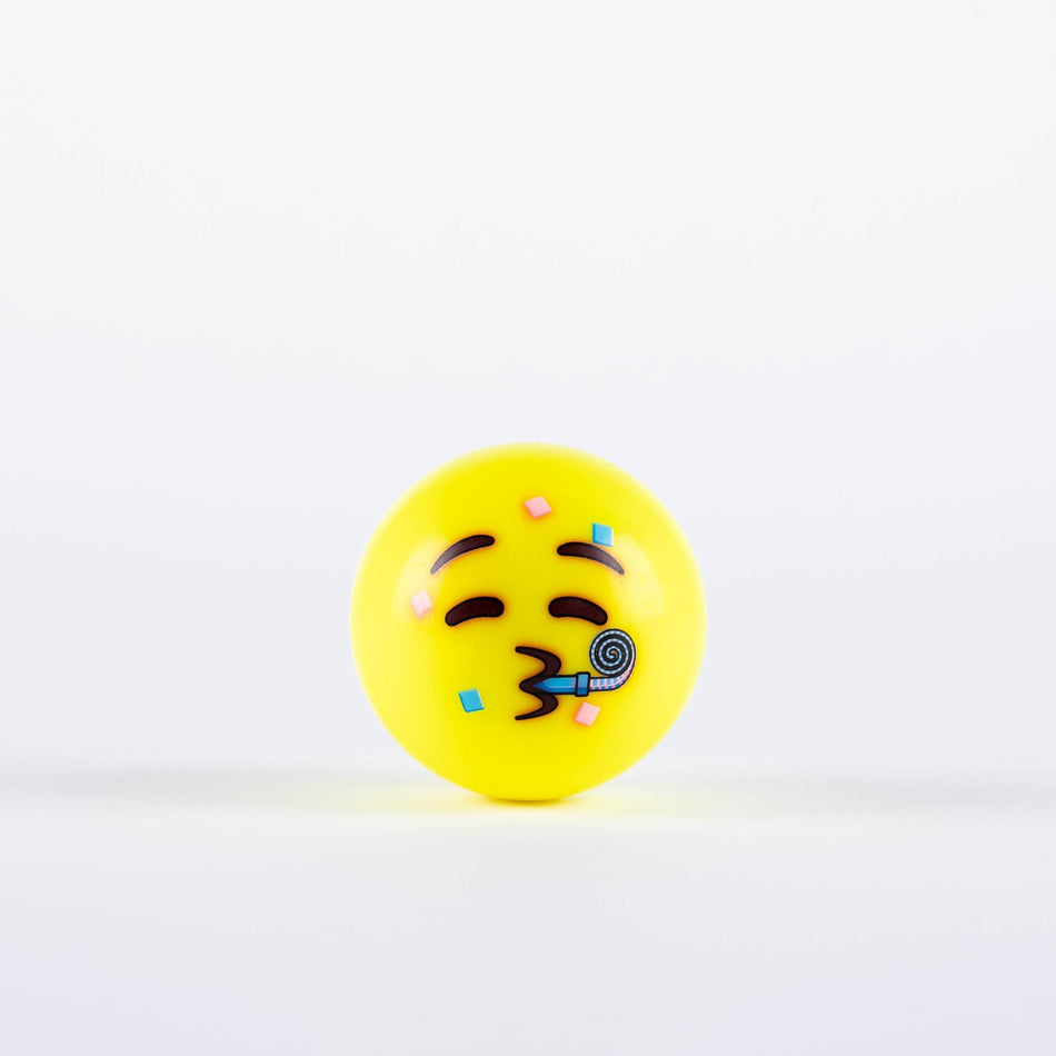 The Grays Emoji Hockey Ball by Grays features a yellow ball with a festive face, closed eyes, arched eyebrows, and pursed lips blowing a party horn with confetti—perfect as a 2025 hockey player gift—on a white background.