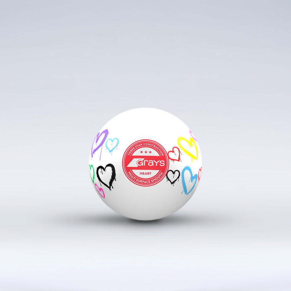 The Grays Novelty Hockey Ball 2026 features a white design with three-star construction, a red central logo, and colorful heart graphics—an eye-catching choice for any hockey player.