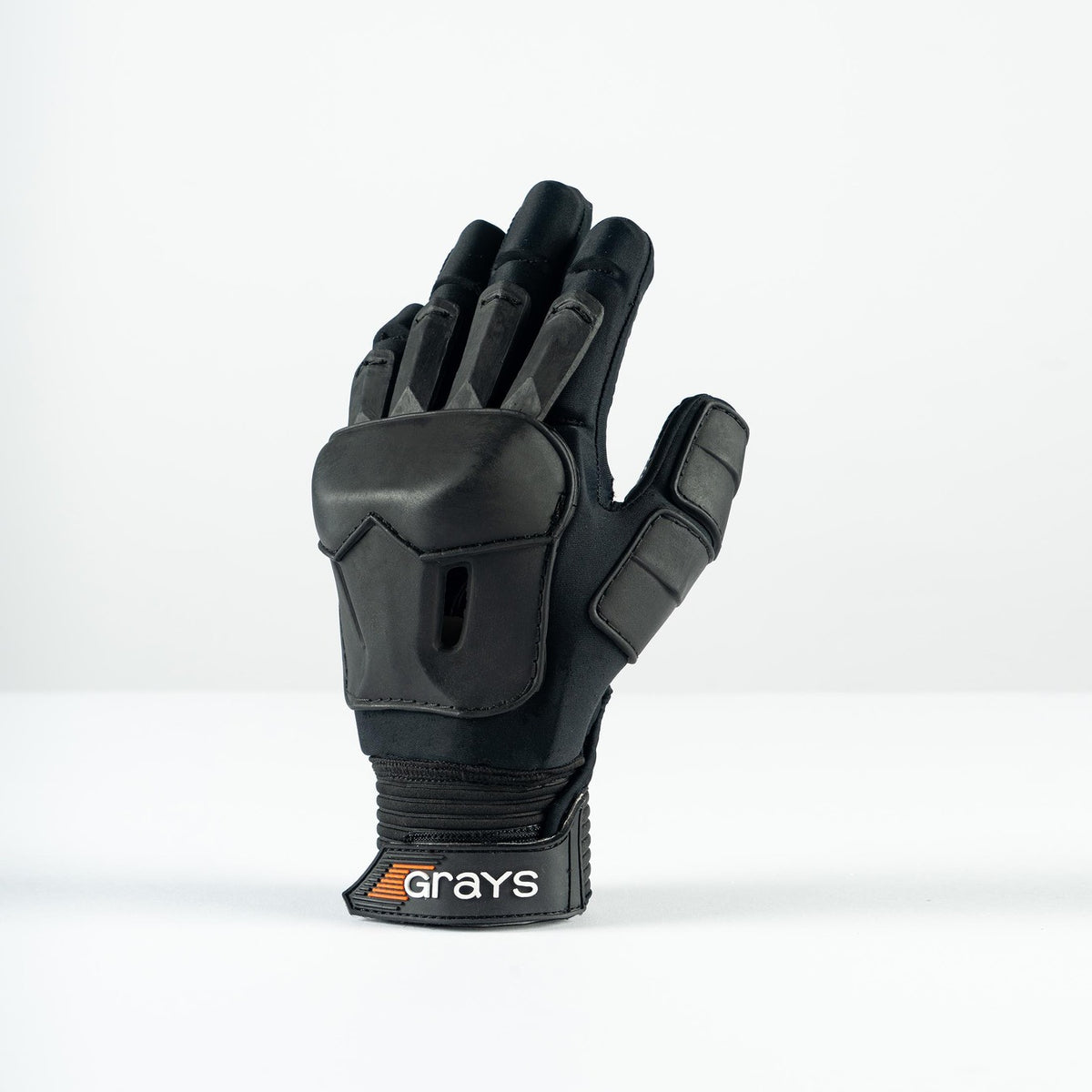 The Grays Prime Full Hockey Glove, in black with FlexShell armour and reinforced padding for top impact absorption on fingers and back, is displayed upright on a white surface. The wrist strap features the Grays brand name.