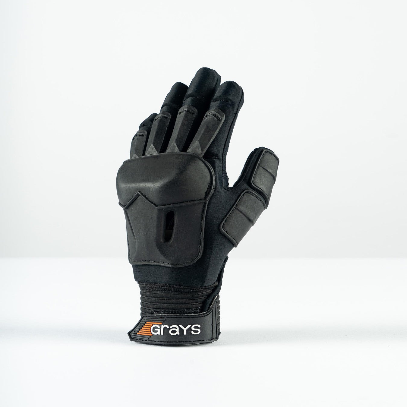 The Grays Prime Full Hockey Glove, in black with FlexShell armour and reinforced padding for top impact absorption on fingers and back, is displayed upright on a white surface. The wrist strap features the Grays brand name.