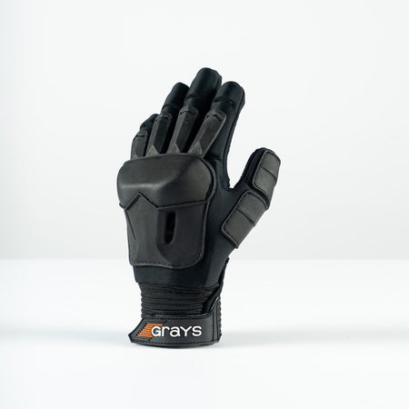 The Grays Prime Full Hockey Glove, in black with FlexShell armour and reinforced padding for top impact absorption on fingers and back, is displayed upright on a white surface. The wrist strap features the Grays brand name.