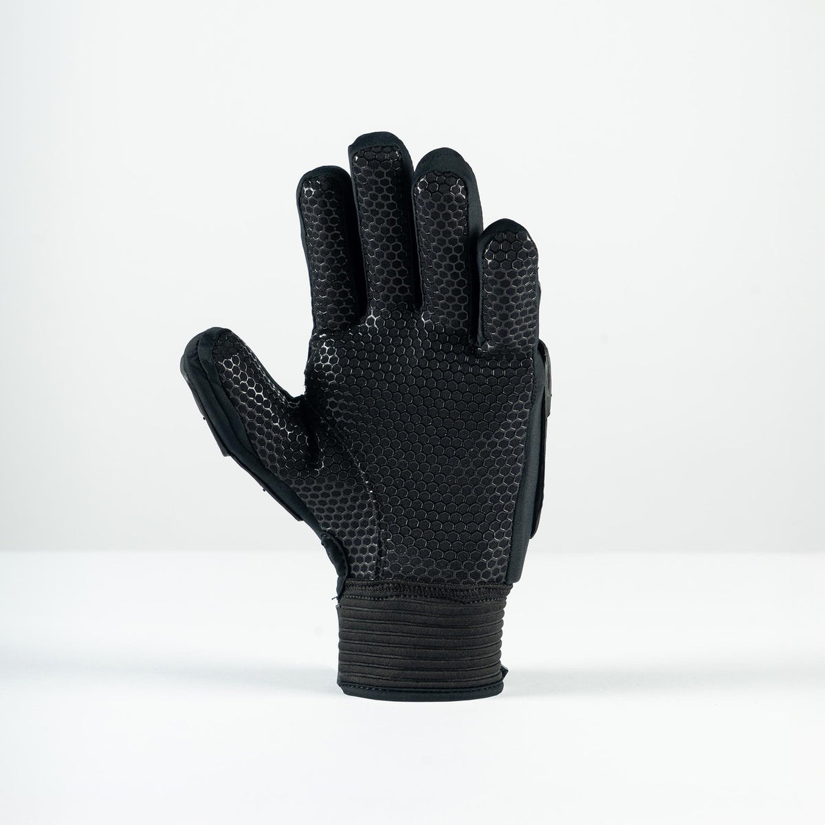The Grays Prime Full Hockey Glove by Grays, featuring a black FlexShell design with a textured honeycomb pattern on the palm and fingers, stands upright on a white surface against a plain white background.