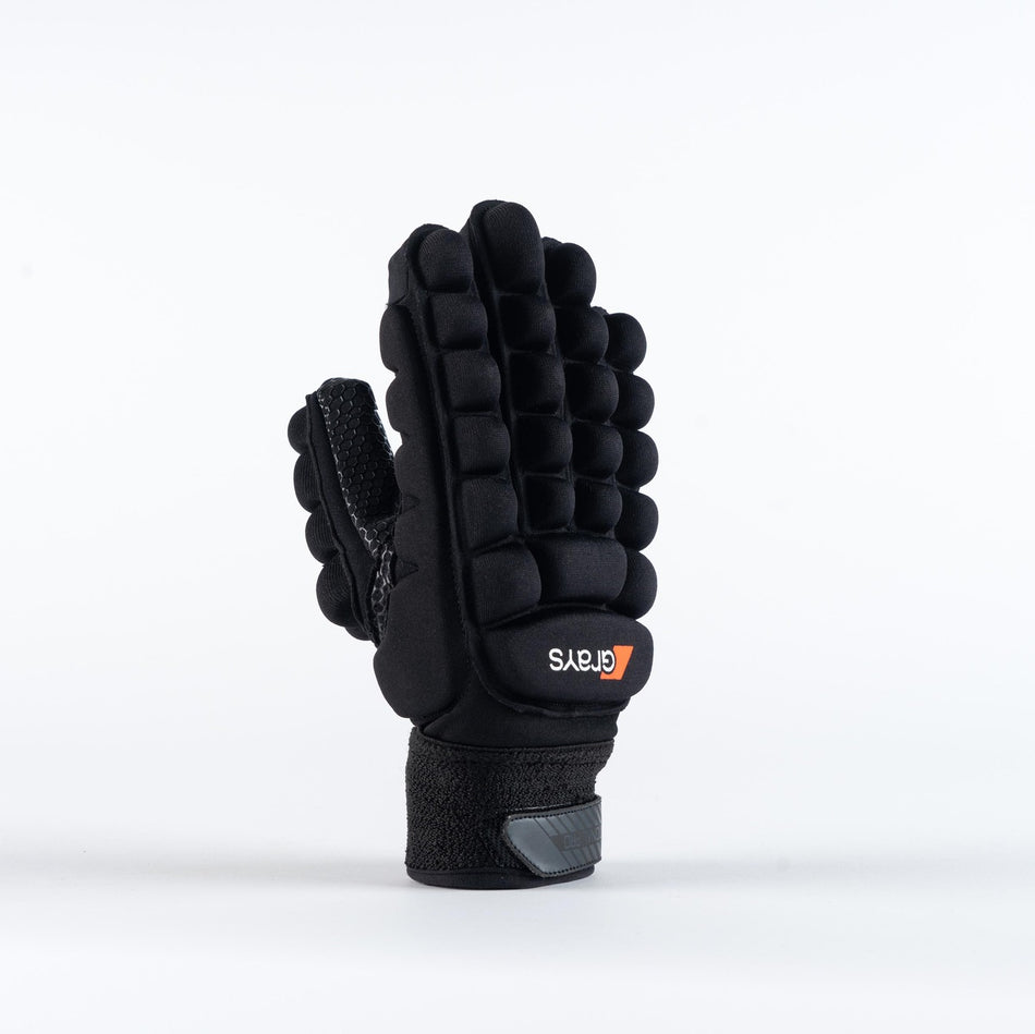 The Grays International Pro Hockey Glove by Grays, in black, is shown standing upright on a plain white background. It features a lycra palm, thick segmented cushioning on the back, Velcro wrist strap, and an orange and white logo.