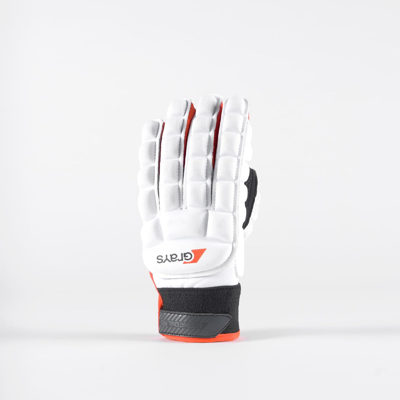 The Grays International Pro Hockey Glove in white stands upright, showcasing full-finger coverage, black and red accents, finger padding, and a lycra palm for flexible, all-weather grip.