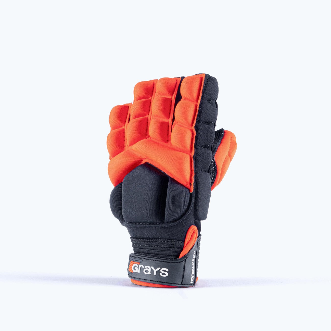 The Grays Apex Touch Hockey Glove, in red, features padding, segmented finger protection, and a half-finger design for all-weather grip. The Grays brand is visible on the wrist strap as the glove stands on a white background.