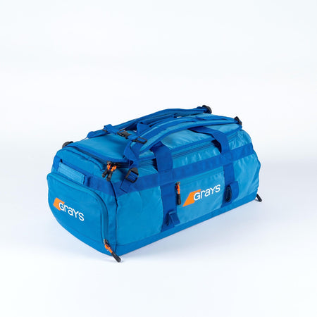 The Grays Omega Gen 4 Holdall is a spacious blue hockey gear bag with the Grays logo in white and orange, multiple zippered compartments, handles, adjustable shoulder straps, and a stick-ready design—ideal for pro players.