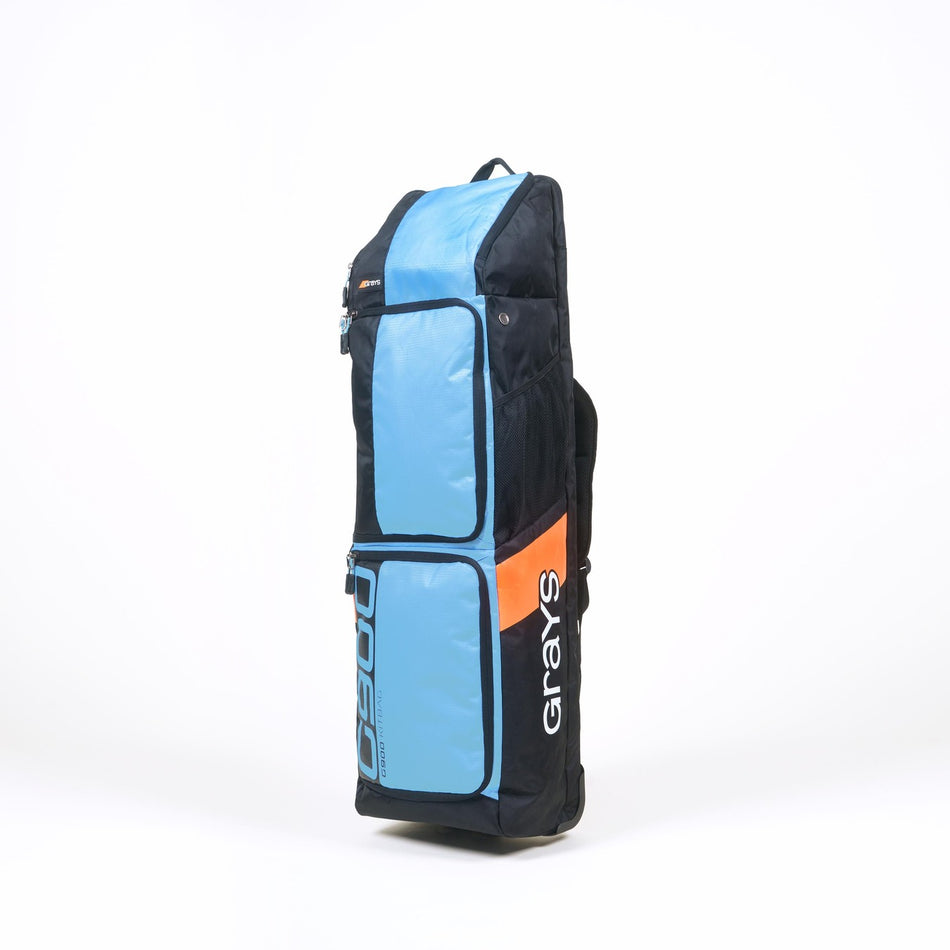 The Grays G900 Hockey Kitbag is a tall, rectangular wheeled duffle with black, light blue, and orange panels, white Grays logo, multiple zippered sections, a padded stick compartment, and a top handle for easy carrying.