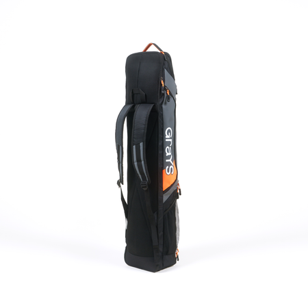 The Grays Delta Gen3 Hockey Kitbag, in black and orange, features shoulder straps, zippers, and a padded stick section. It stands upright on a white background with the "Grays" logo displayed on the side.
