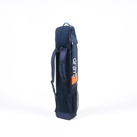 The Grays Delta Gen3 Hockey Kitbag by Grays, in navy blue with orange accents, features shoulder straps, a padded stick section, side pocket, and top handle; it stands upright against a white background.