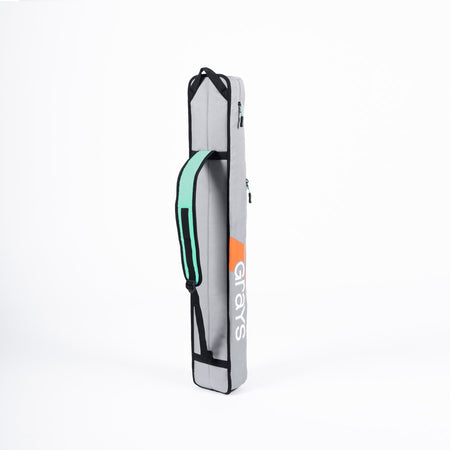 The Grays G100 Hockey Stick Bag is a light gray rectangular kit bag with black edges, a mint green and black single strap, and "Grays" in white and orange on the side. It features a stick section and stands upright against a white background.