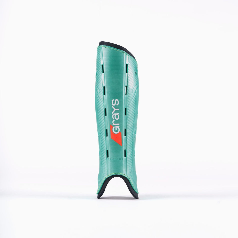 An aqua and black Grays G600 Hockey Shinguard stands upright on a white background, featuring the Grays logo in the center. Its lightweight polymer shell delivers excellent impact protection.