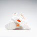 The Grays Stealth 1.0 Hockey Shoes in white, by Grays, are shown on a plain white background—one upright and one on its side to highlight the textured high-performance outsole and orange detailing.