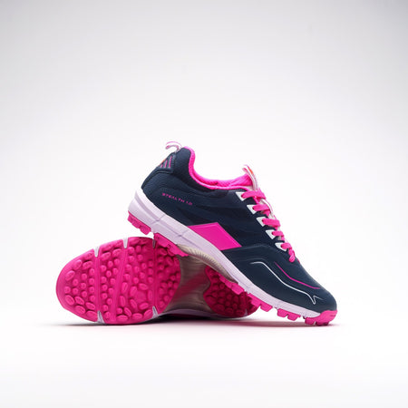 The Grays Stealth 1.0 Hockey Shoes by Grays feature navy uppers, bright pink accents, white soles, and pink textured outsoles. One shoe stands while the other leans to reveal their high-grip performance rubber sole.
