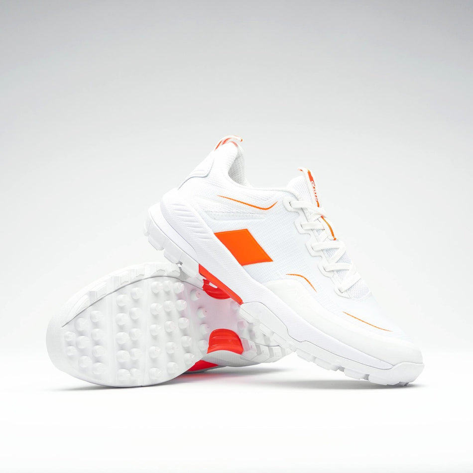 The Grays Aero Cage X Hockey Shoes by Grays are white athletic shoes with bright orange accents and a genius foam midsole for lightweight comfort. Displayed on a plain background, one shoe is upright and the other lies on its side.