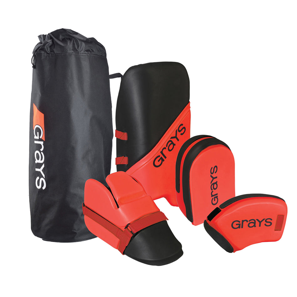 The Grays G100 Goalie Set - Senior, in red and black, includes dual-density foam leg guards, hand protectors, a helmet, and comes with a black Grays-branded drawstring bag.