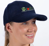 A person wearing a Gray Nicolls Heavy Rollers CC Melton County Cap in navy, senior size, with "The New Rollers" embroidered in green and red. They're smiling and gazing slightly to the side.
