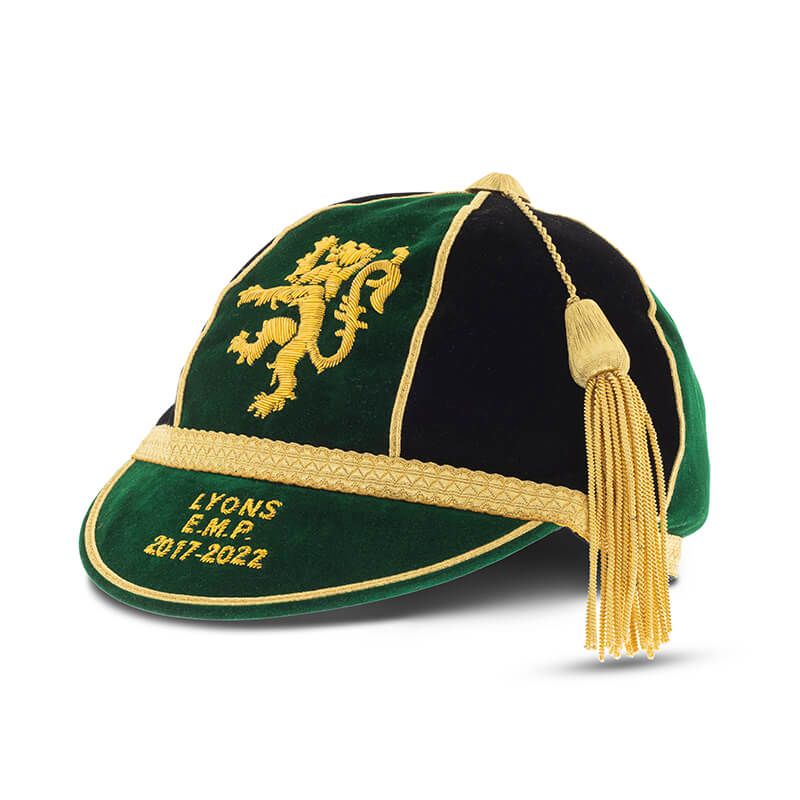 A custom green and black velvet honour cap with gold trim, lion embroidery, LYONS E.M.P 2017-2022 text, and a gold tassel from Martin Berrill Sports—ideal for commemorative or bespoke cricket caps.