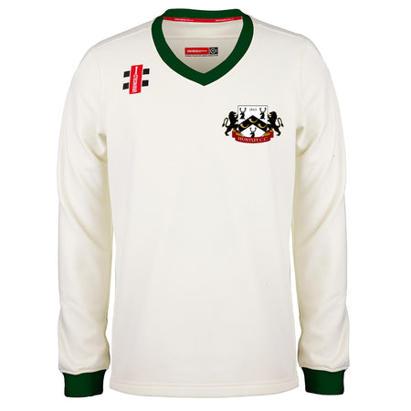The Gray Nicolls Huntley CC Pro Performance Sweater (Junior) is a long-sleeved, off-white cricket sweater with green V-neck and cuff trim, lion crest on the left chest, and red/black right shoulder patches—ideal for pro-level matches.