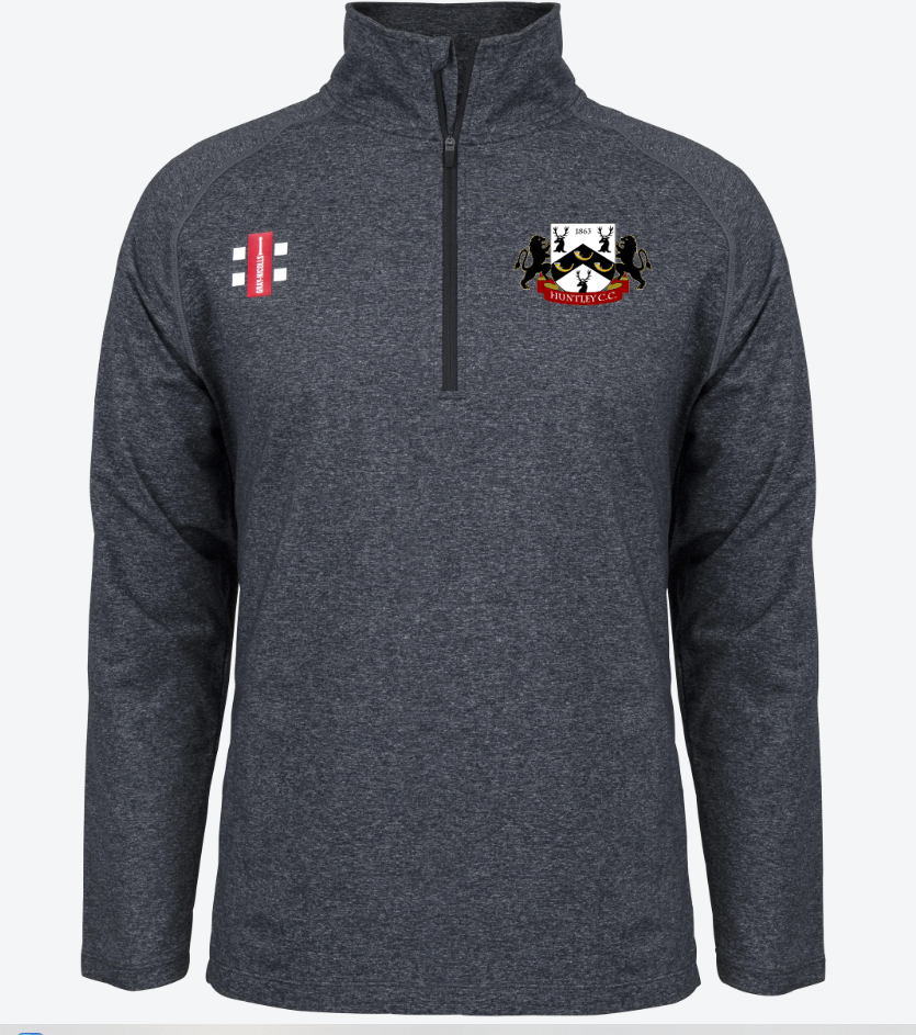 The Huntley CC Velocity Mid Layer by Gray Nicolls is a dark gray stretch-fit quarter-zip pullover, featuring a red and white cricket logo on the right chest and a multicolored club crest with black birds and a shield on the left.