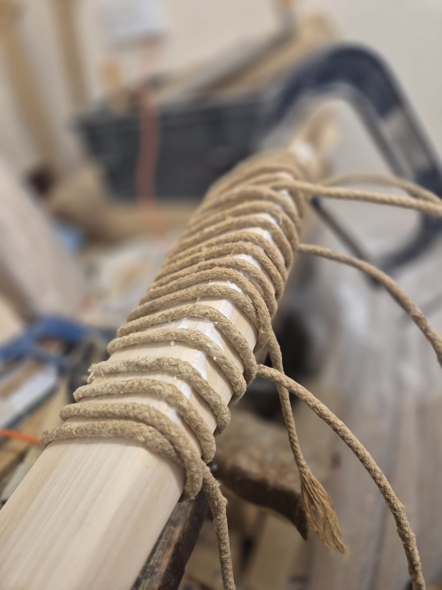 A close-up of the Cricket Bat Repair - Pre Season & End of Season Clean up by Martin Berrill Sports, showing wooden pieces tightly bound with rope for bat restoration, with tools and materials blurred in the background.
