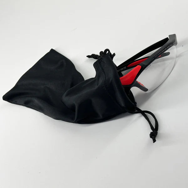 A pair of Karakal Adult Pro 3000 Sports Eye Protection goggles by Karakal, featuring clear anti-fog polycarbonate lenses and black-and-red frames, is partially pulled from a black drawstring pouch on a white surface.